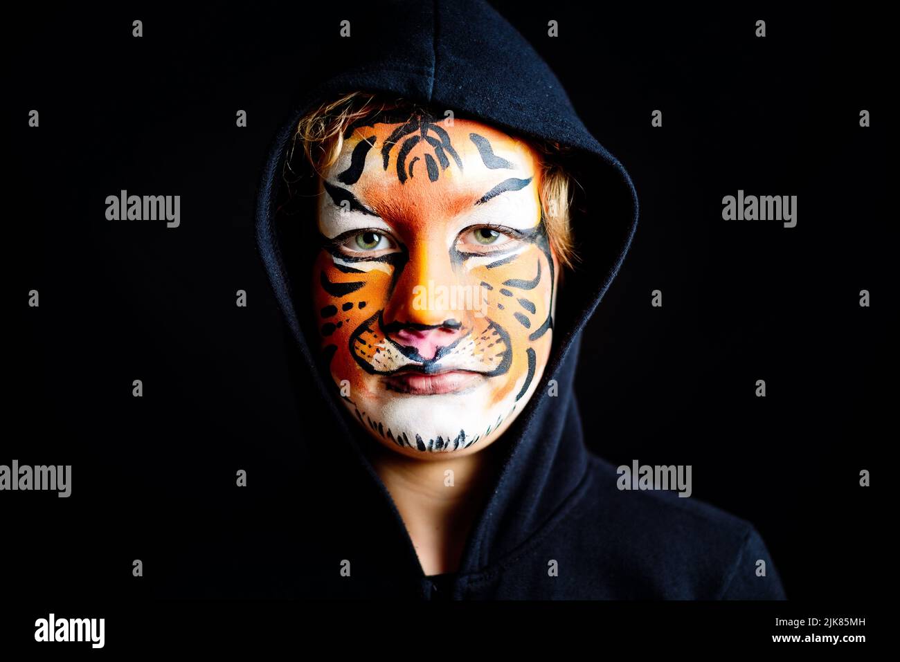 Regard mystérieux d'un enfant avec le caractère félin, peint le visage d'un tigre dangereux, sérieux, isolé sur fond noir. Banque D'Images