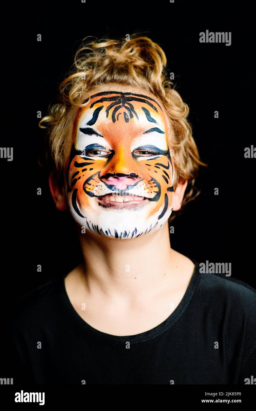 Portrait d'un garçon avec visage de tigre peint avec une expression heureuse, isolé sur fond noir. Banque D'Images