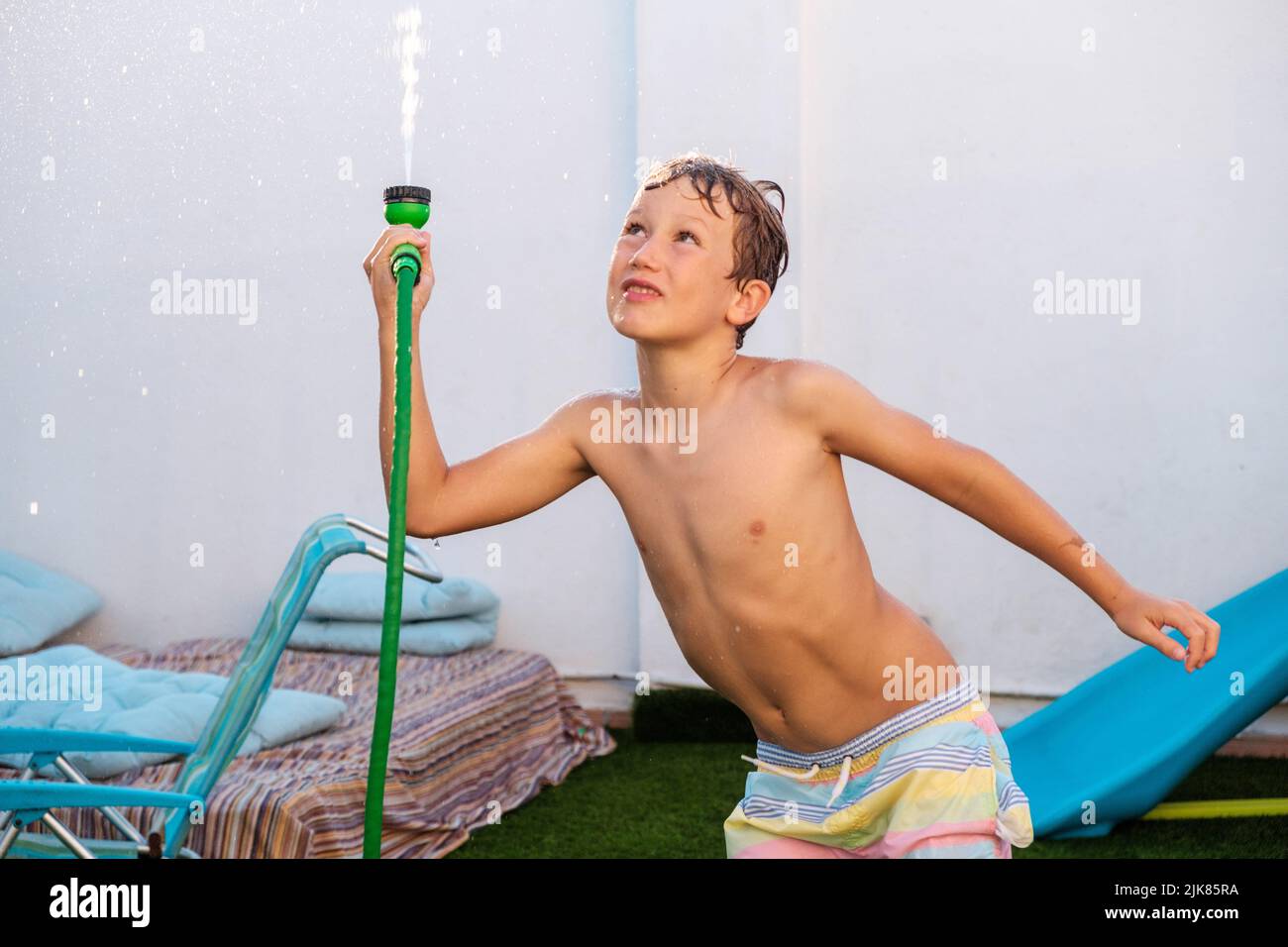 Enfant jouant avec un tuyau pour se rafraîchir avec de l'eau pendant une vague de chaleur estivale en Europe. Banque D'Images