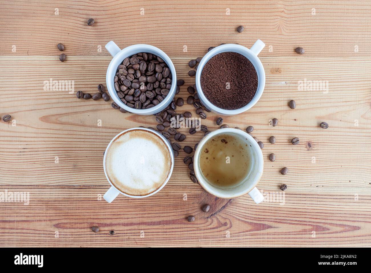 Quatre tasses de café. Un avec des grains de café, un avec des grains de café moulus, un avec du café avec du lait et un avec une tasse vide sur une table en bois Banque D'Images