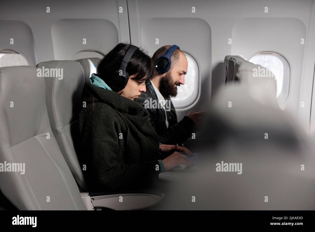 Jeunes voyageurs utilisant un ordinateur portable et un smartphone en avion, attendant d'arriver aux vacances. Deux passagers travaillant sur des appareils et voyageant avec une compagnie aérienne internationale. Banque D'Images