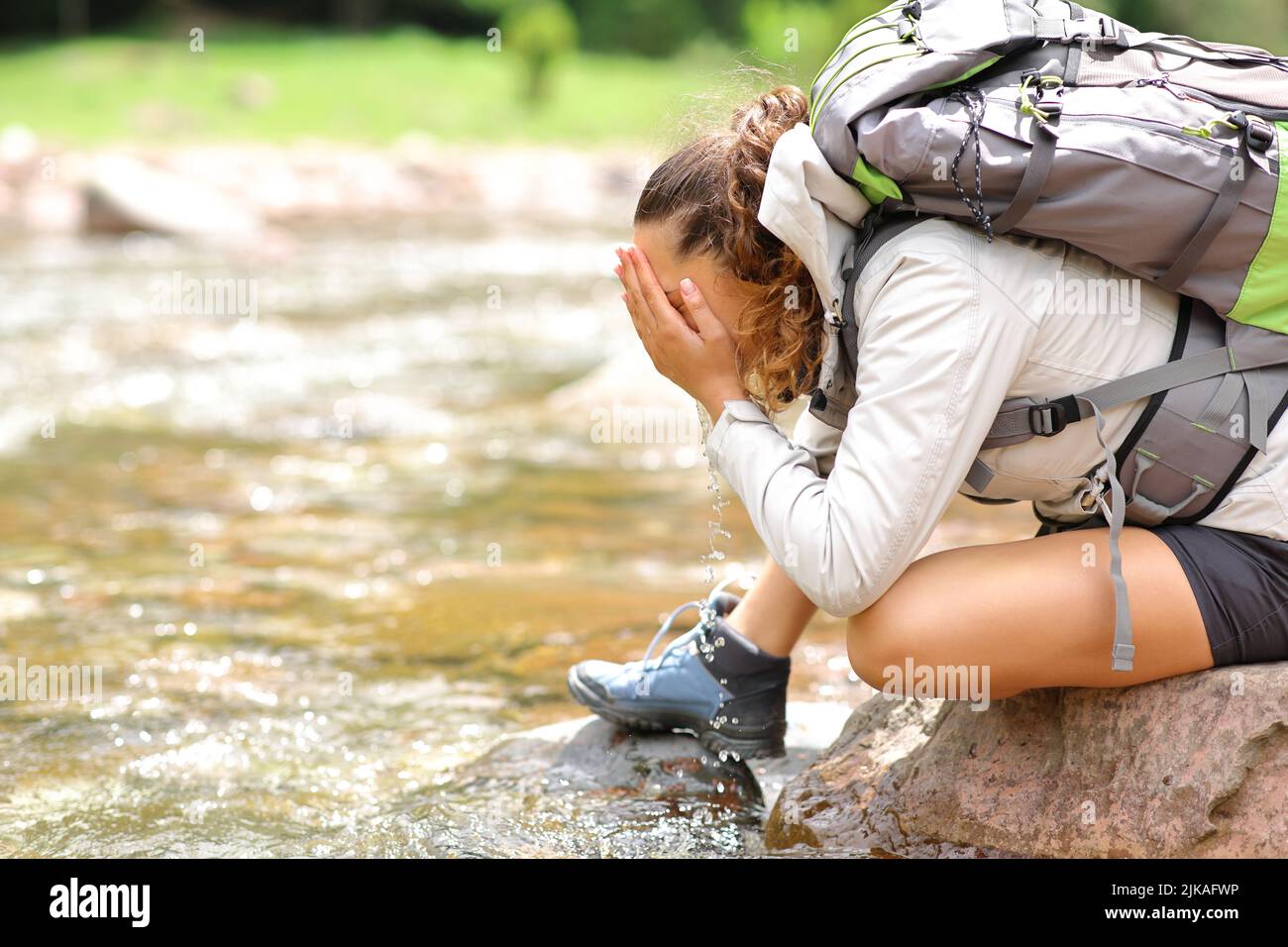 Profil d'une femme de trekker nettoyant le visage dans une rivière dans la montagne Banque D'Images