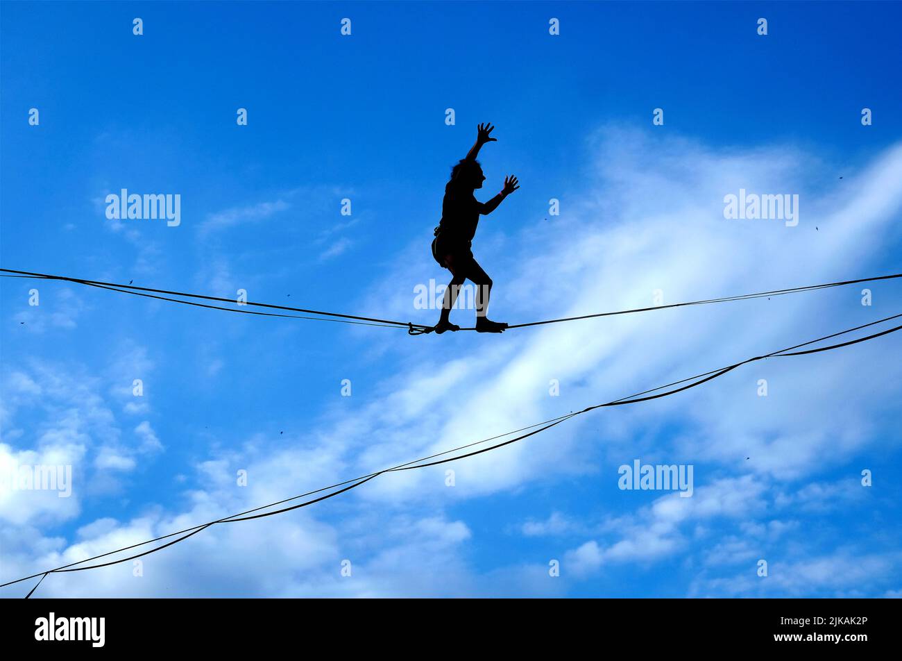 Lublin, Pologne 29 juillet 2022. Silhouette d'un jeune homme qui marche sur une corde raide contre un ciel bleu au festival Urban Highline Banque D'Images