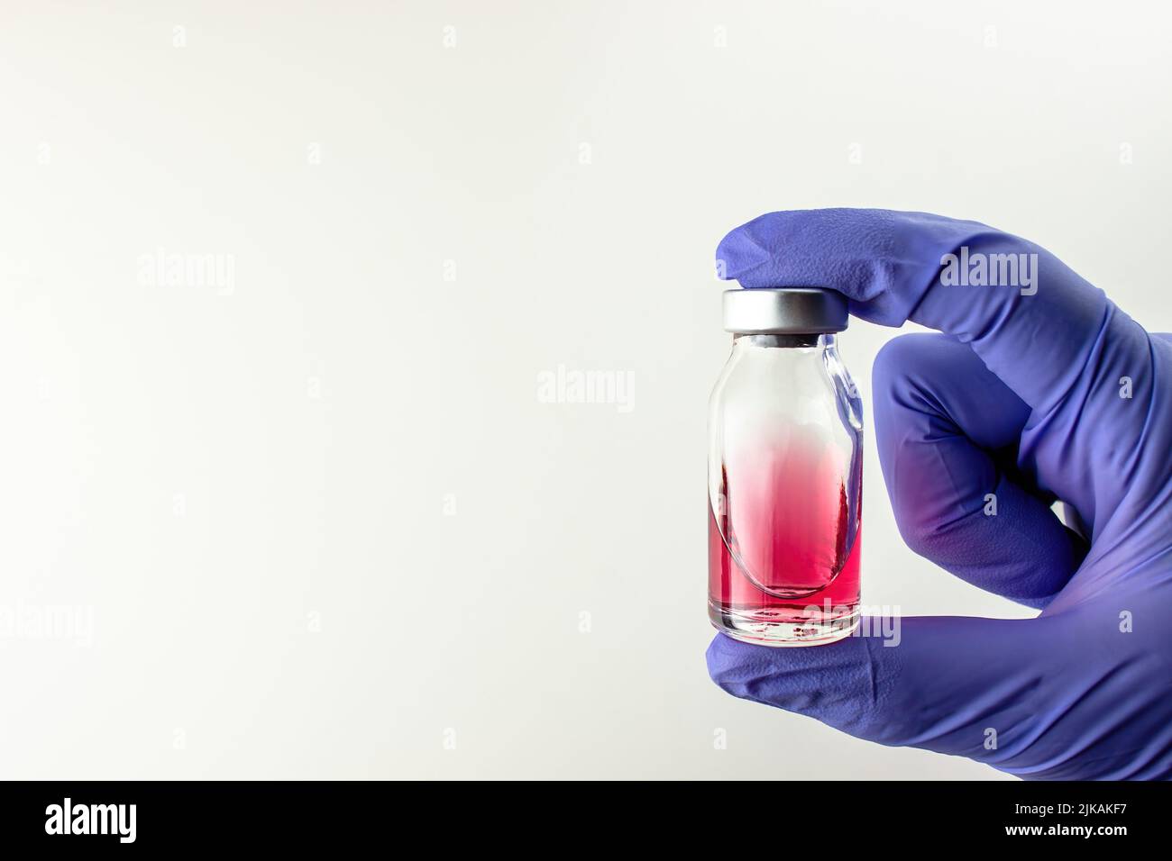 Liquide rouge (vitamine B12) dans une ampoule en verre avec un bouchon dans la main dans un gant médical bleu sur fond blanc. Beaucoup d'espace vide Banque D'Images
