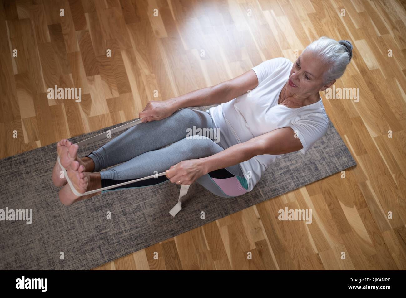 Femme caucasienne senior faisant des exercices d'abs, assis dans le bateau yoga pose à la maison. Banque D'Images