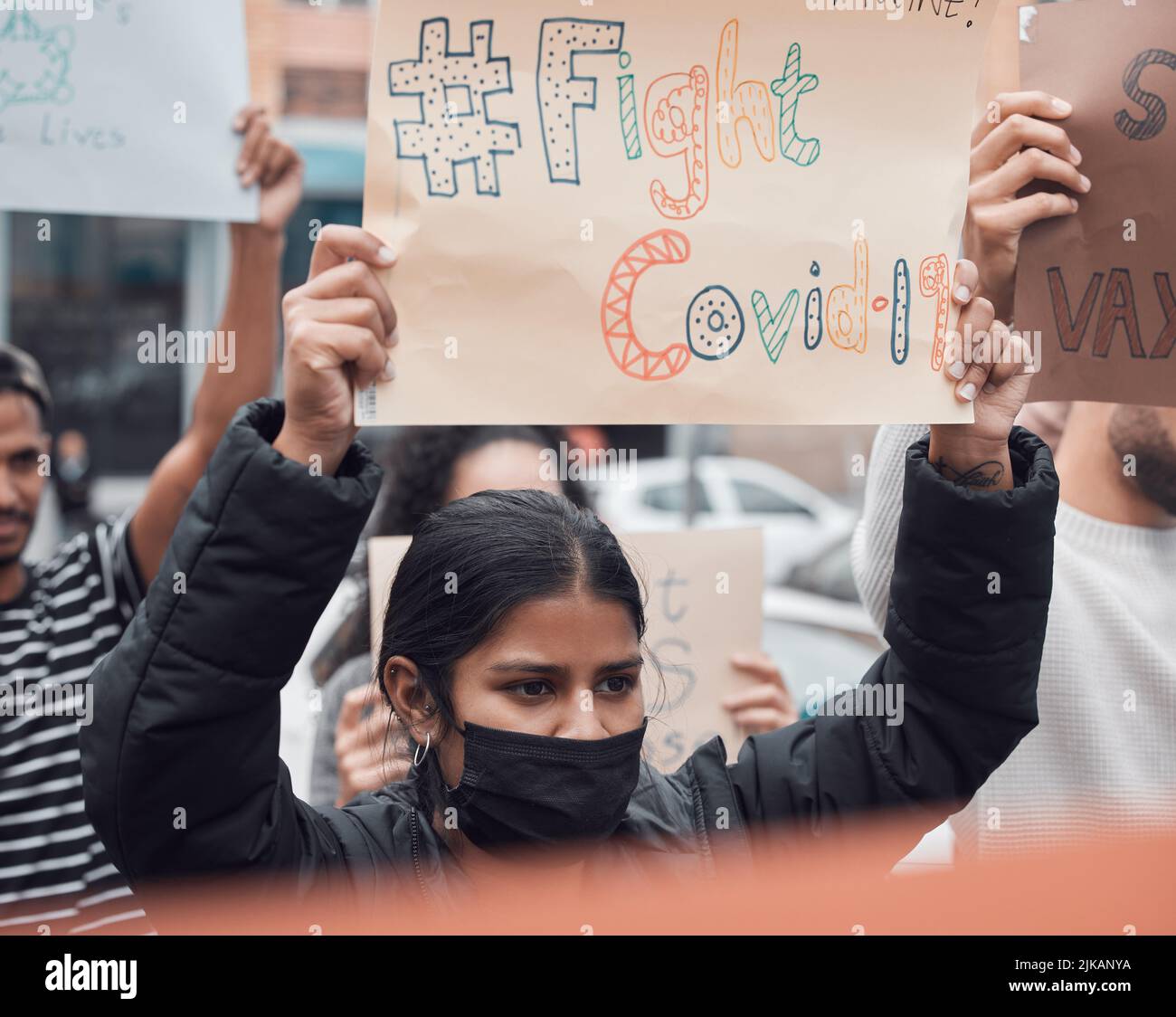 Combattez le covid. Une jeune femme attrayante tenant un panneau protestant contre le vaccin contre le covid 19 avec d'autres manifestants en arrière-plan. Banque D'Images