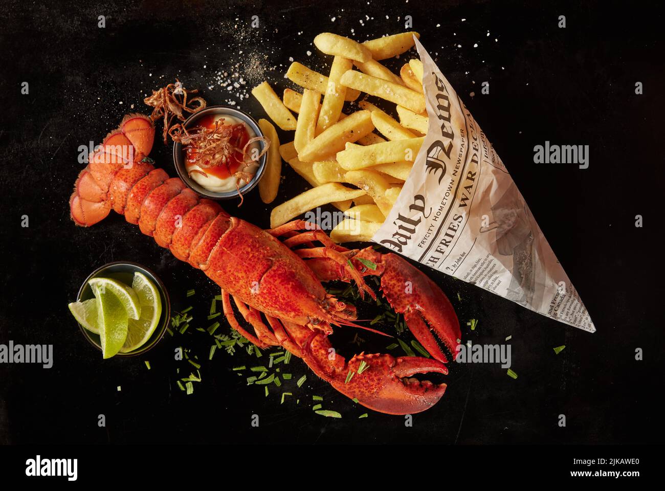 Vue de dessus de délicieux homard rouge et chips de pomme de terre dans un journal, servi avec de la sauce et des herbes près des tranches de lime sur fond noir Banque D'Images
