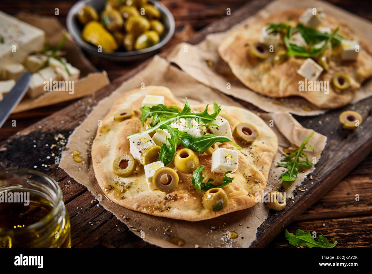 Grand angle de pain plat fraîchement cuit avec des morceaux de fromage de feta assaisonnés olives et rucola servis sur le plan de coupe près de l'ingrédient dans la cuisine Banque D'Images