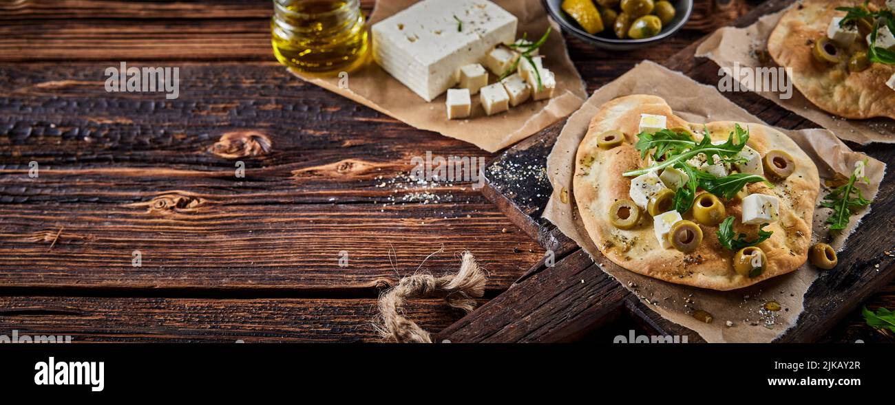 De dessus de délicieux pain pita croustillant avec des olives au fromage feta et de la rocola servi sur une planche à découper en bois sur table dans la cuisine Banque D'Images