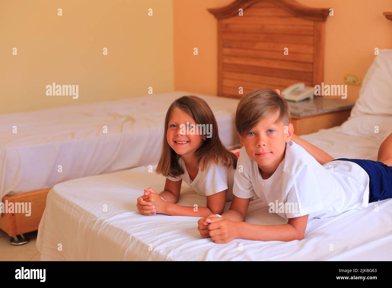 En vacances, deux enfants s'étendent sur un lit avec des draps blancs dans une chambre d'hôtel. Les enfants jouent sur le lit avec des draps blancs à la maison. Garçon et fille avant d'aller au lit à la maison Banque D'Images