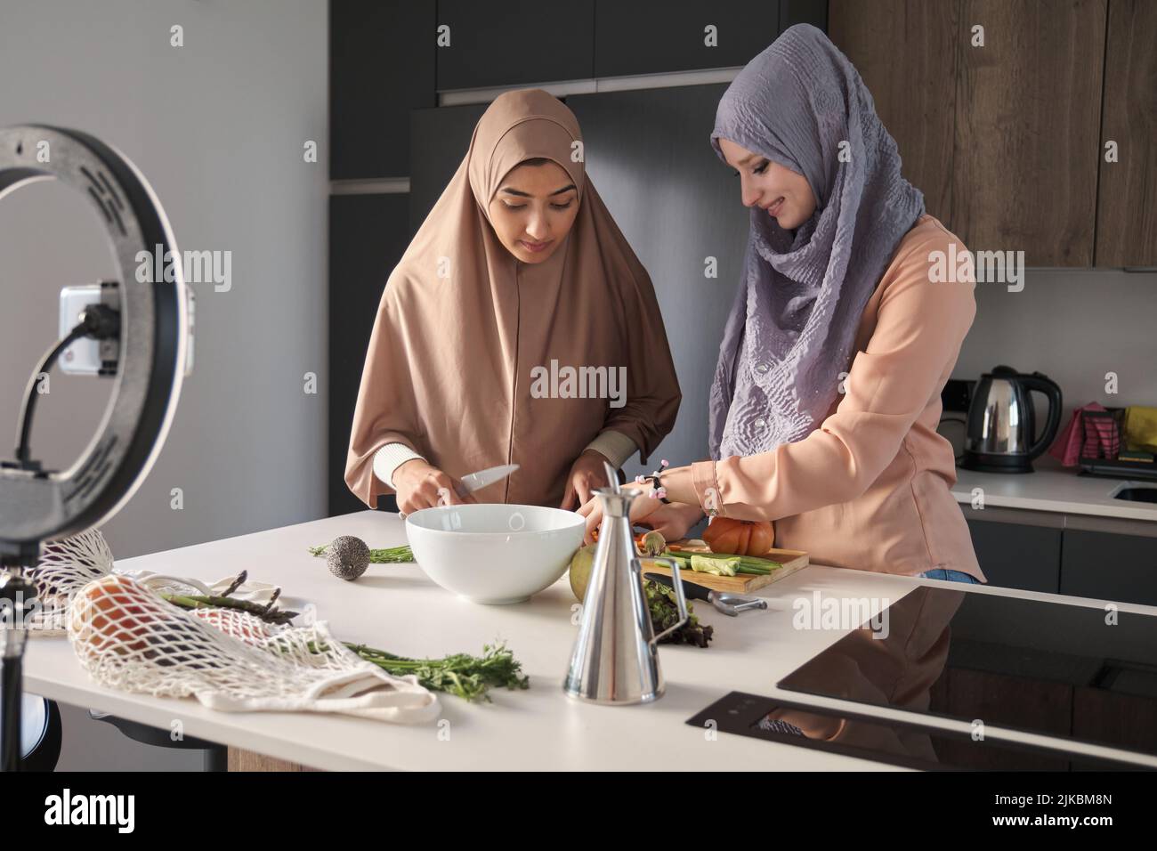 Deux enregistreurs de nourriture musulmans faisant une vidéo tout en préparant des légumes dans la cuisine. Banque D'Images
