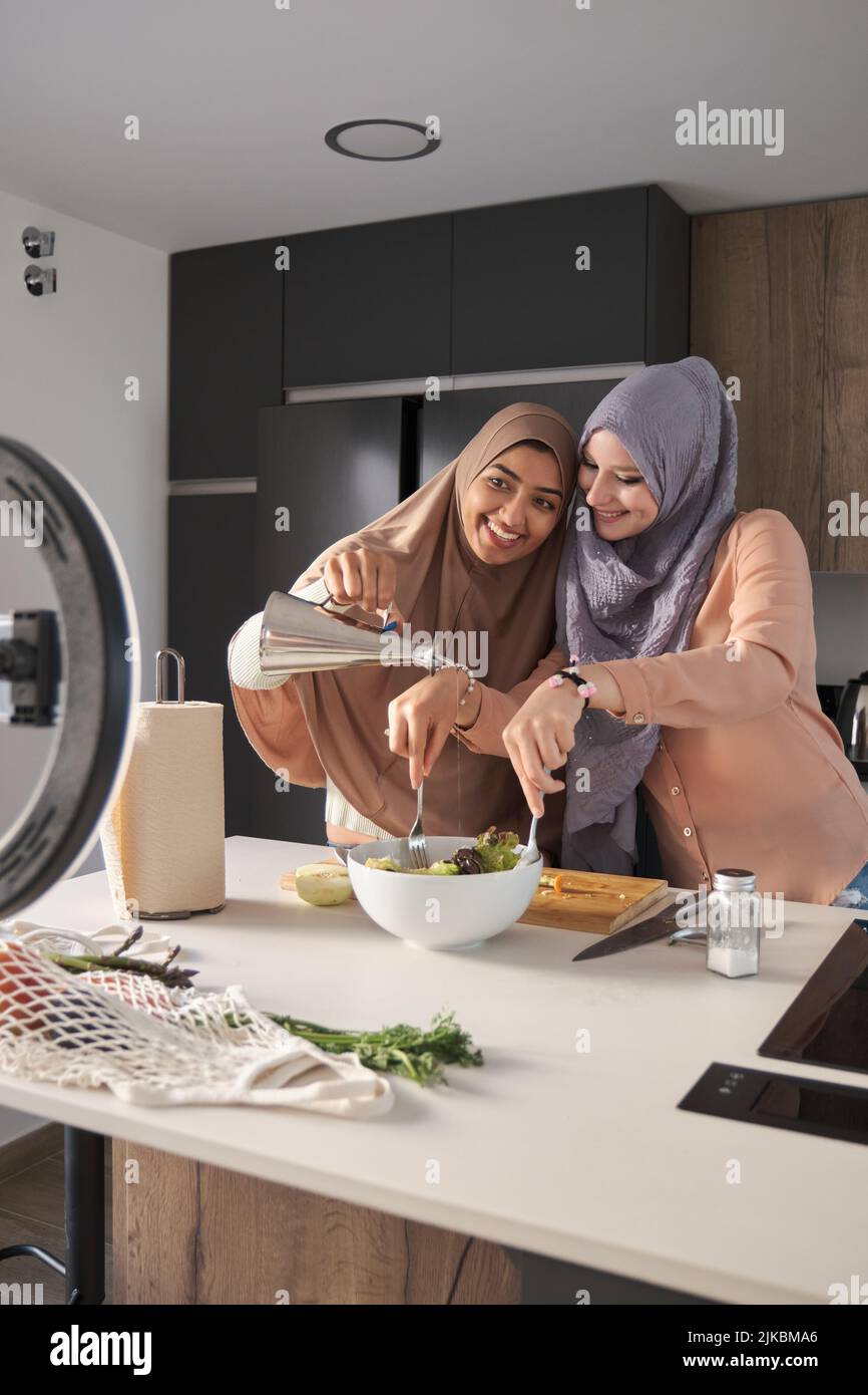 Deux bûcherons musulmans souriant tout en versant de l'huile d'olive dans une salade dans la cuisine. Banque D'Images