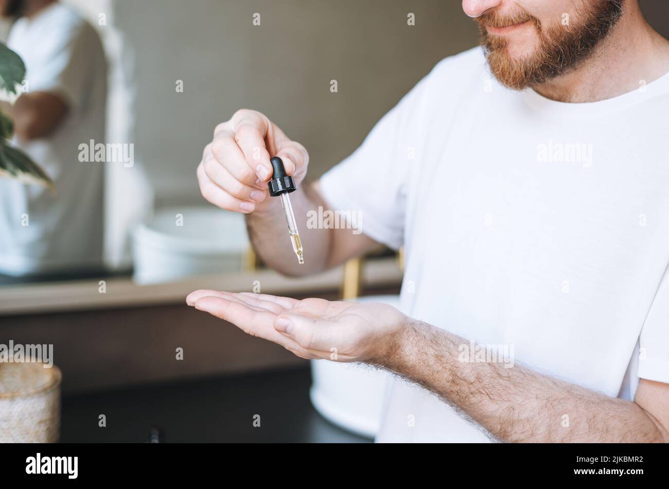 Homme beau adulte avec pipette avec huile de barbe dans la salle de bains à la maison Banque D'Images