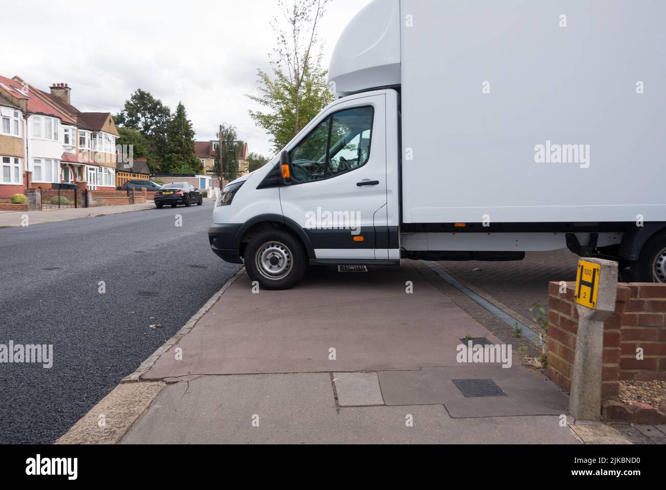Une fourgonnette blanche bloque le chemin de la chaussée dans la zone résidentielle, ce qui force le piéton à emprunter la route Banque D'Images