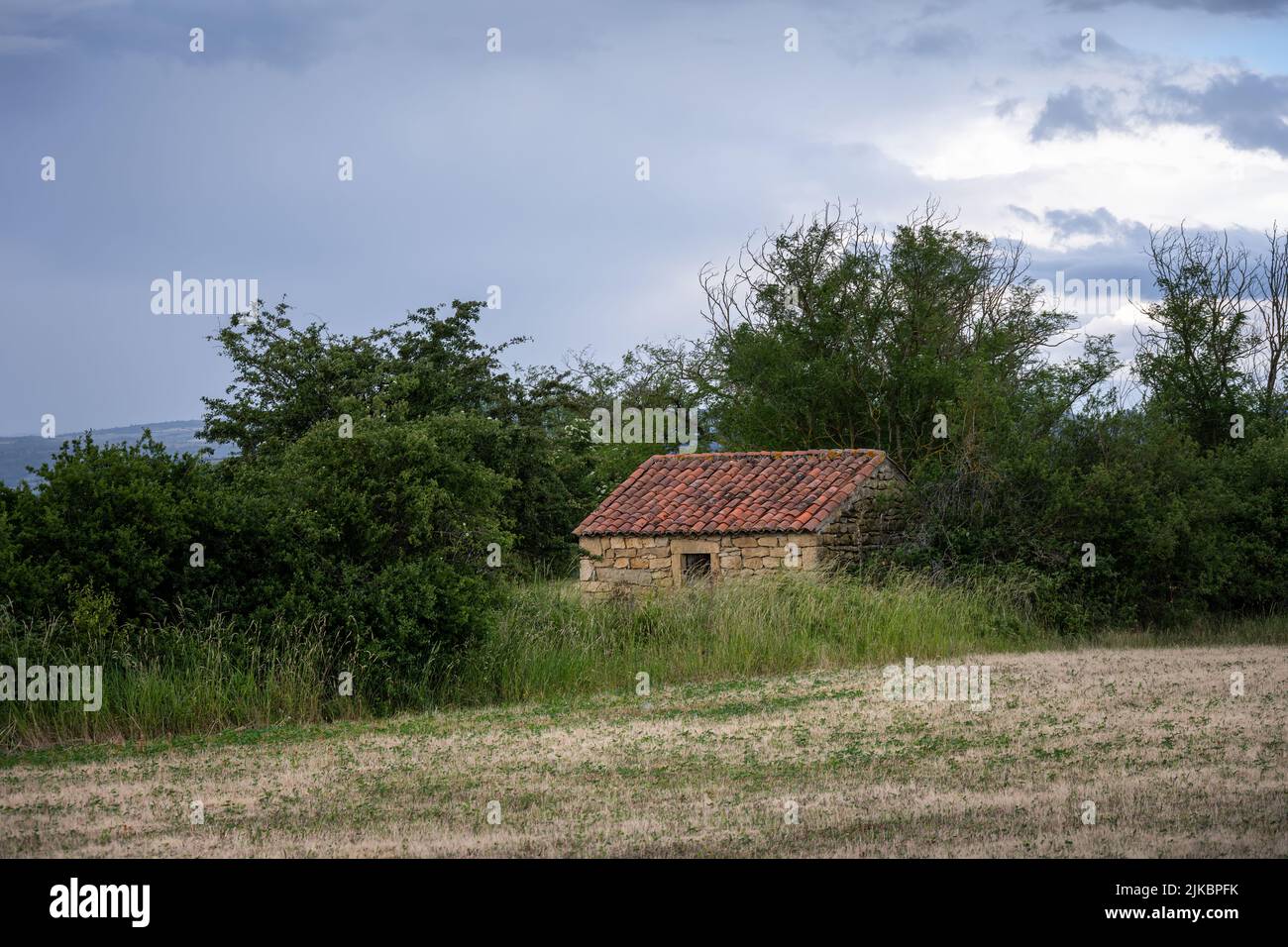 Cabane en pierre dans un champ par un ciel nuageux de printemps, Auvergne, France Banque D'Images