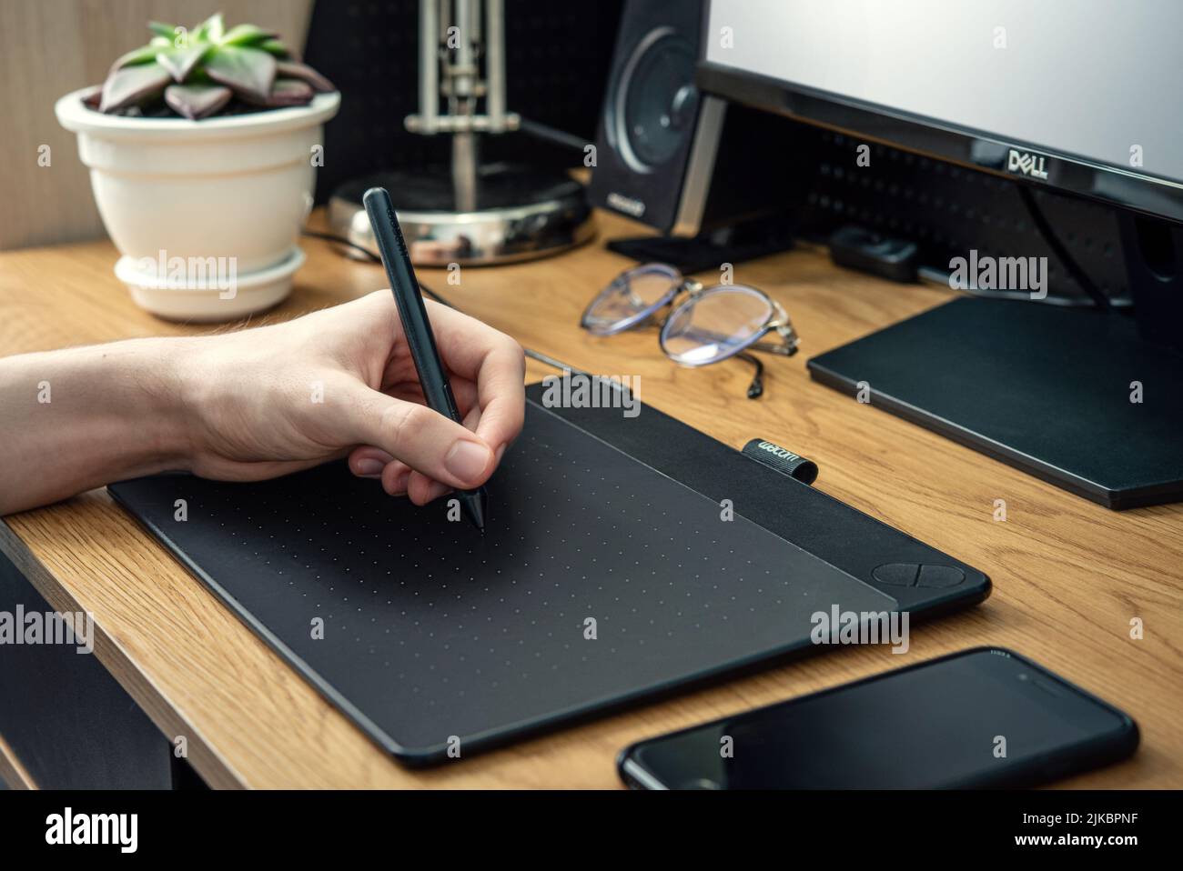 KIEV, UKRAINE - 21 DÉCEMBRE 2021: Jeune graphiste homme utilisant la tablette graphique Wacom sur table noire à la maison de bureau de fermer. Banque D'Images