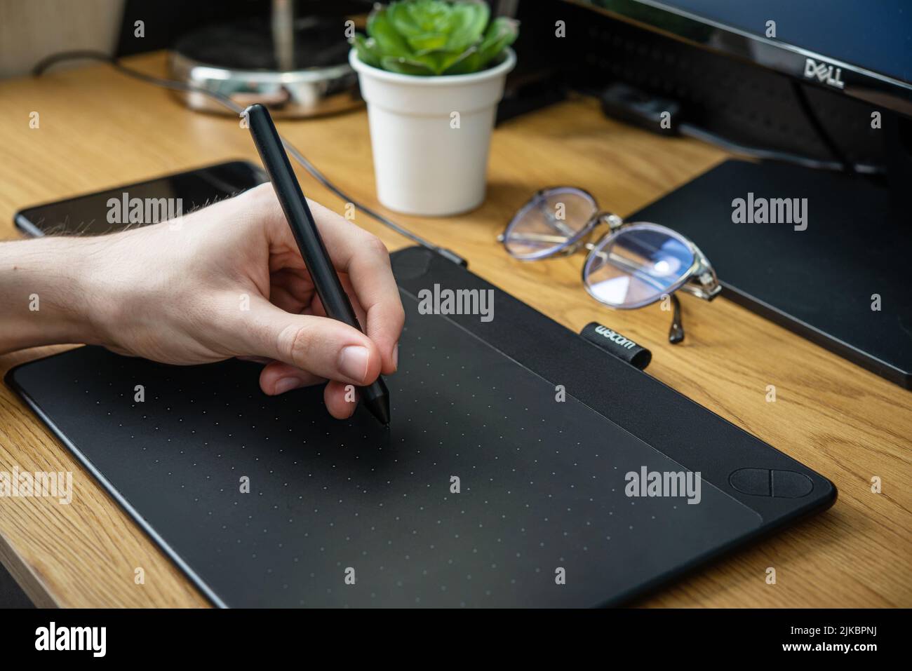 KIEV, UKRAINE - 21 DÉCEMBRE 2021: Jeune graphiste homme utilisant la tablette graphique Wacom sur table noire à la maison de bureau de fermer. Banque D'Images