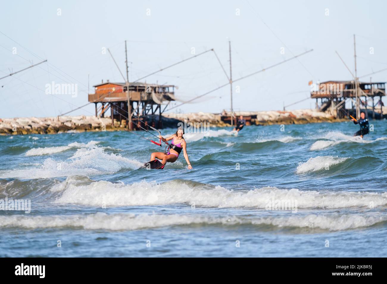 Kite surf fille en maillot de bain avec kite dans le ciel passe les vagues avec l'eau de barbotage. Sports nautiques, femme sportive, concept d'action et sport dur Banque D'Images