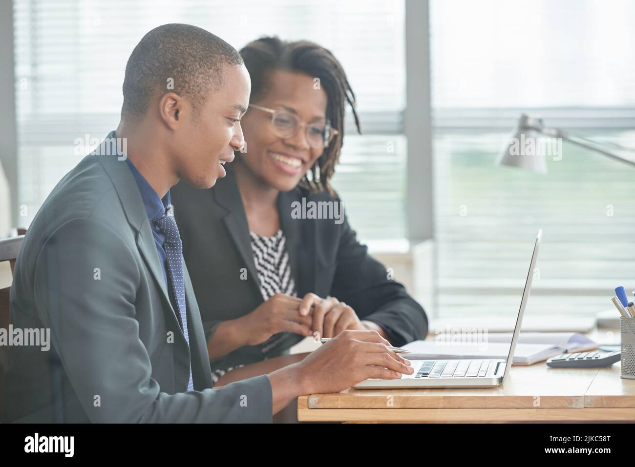 Une équipe de gestionnaires financiers joyeux, assis au bureau et préparant des comptes annuels avec un ordinateur portable, à l'intérieur du bureau ouvert en arrière-plan Banque D'Images