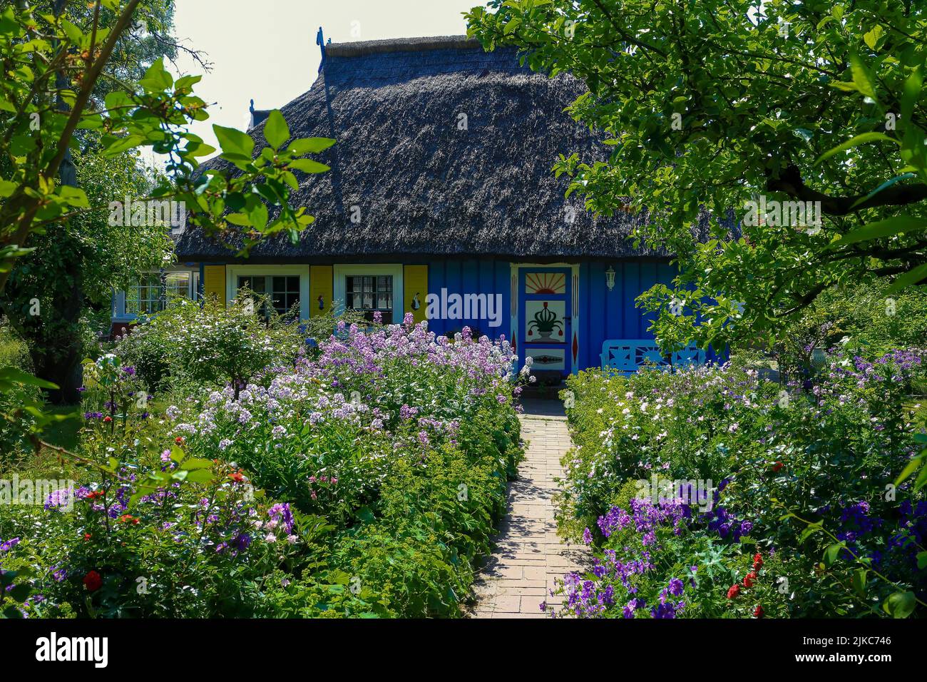 Sentier à travers de magnifiques parterres de fleurs jusqu'à une ancienne maison en bois avec un toit de chaume Banque D'Images