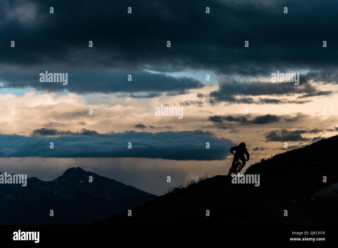 Mountain Biker en virage sur Ridgeline dans Loomy Alpine Vista Banque D'Images