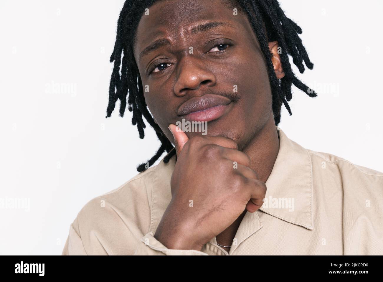 Jeune homme noir avec des dreadlocks regardant de côté tout en tenant son menton isolé sur fond blanc Banque D'Images