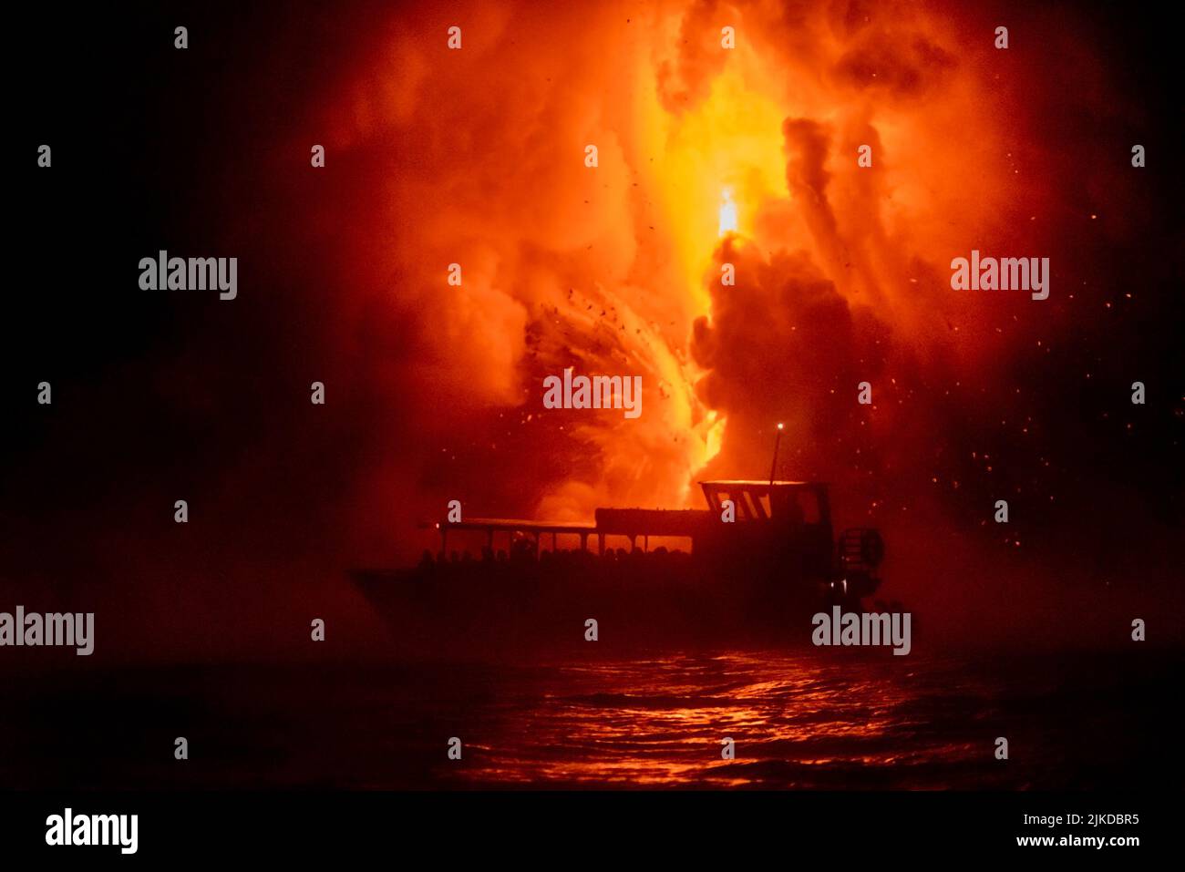 Un bateau touristique flotte en face de l'explosion de lave la nuit, donnant aux gens une vue sur la nature de mère dans sa fureur. Banque D'Images