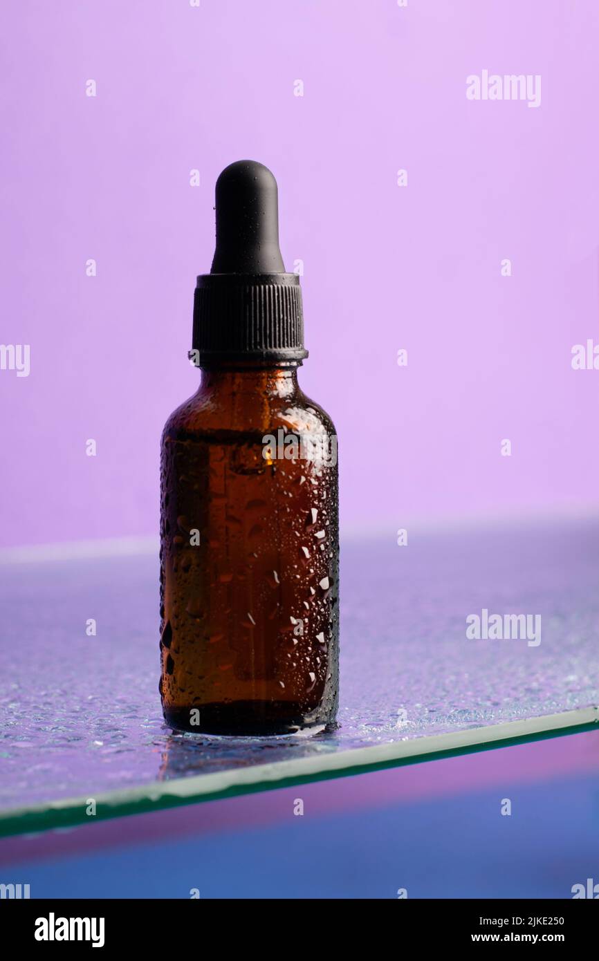Bouteille de produit cosmétique, verre foncé avec pipette sur étagère en verre, fond violet, regarder vers le haut Banque D'Images