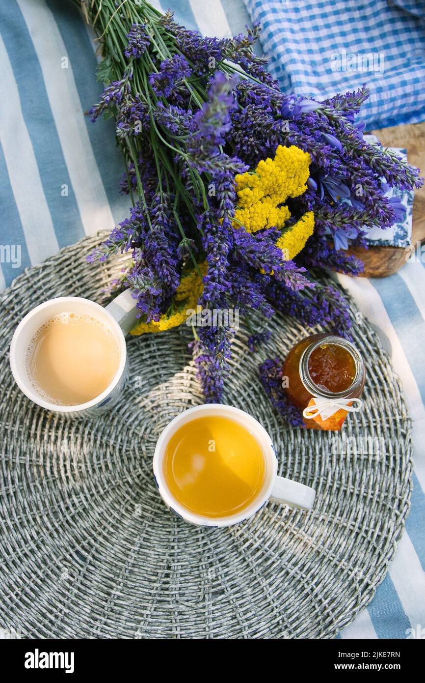 bouquet d'été d'yarrow jaune et de lavande violette, 2 tasses de thé au lait et un pot de confiture de mandarine sur une couverture de pique-nique rayée avec une atmosphère d'été Banque D'Images