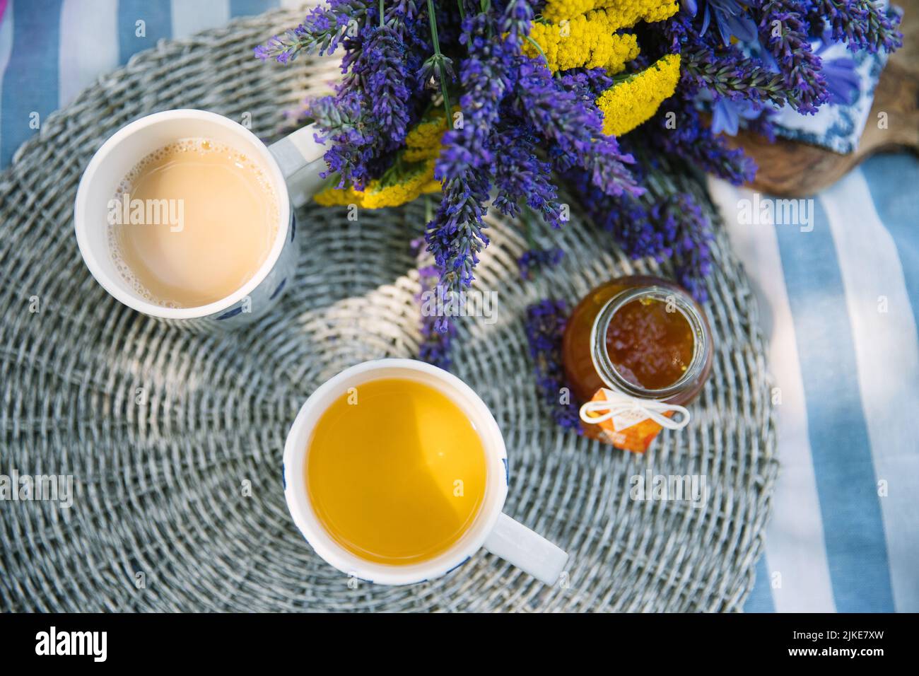 bouquet d'été d'yarrow jaune et de lavande violette, 2 tasses de thé au lait et un pot de confiture de mandarine sur une couverture de pique-nique rayée avec une atmosphère d'été Banque D'Images