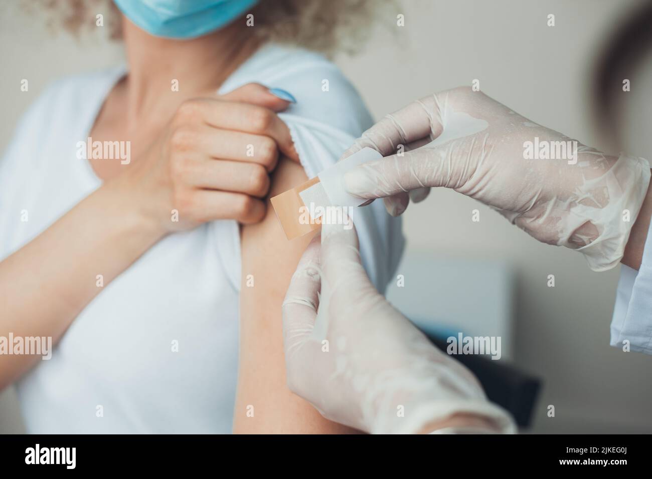 Médecin en gants de protection mettant un bandage adhésif sur le bras de la jeune femme après l'injection du vaccin. La vaccination contre le coronavirus alors que COVID Banque D'Images