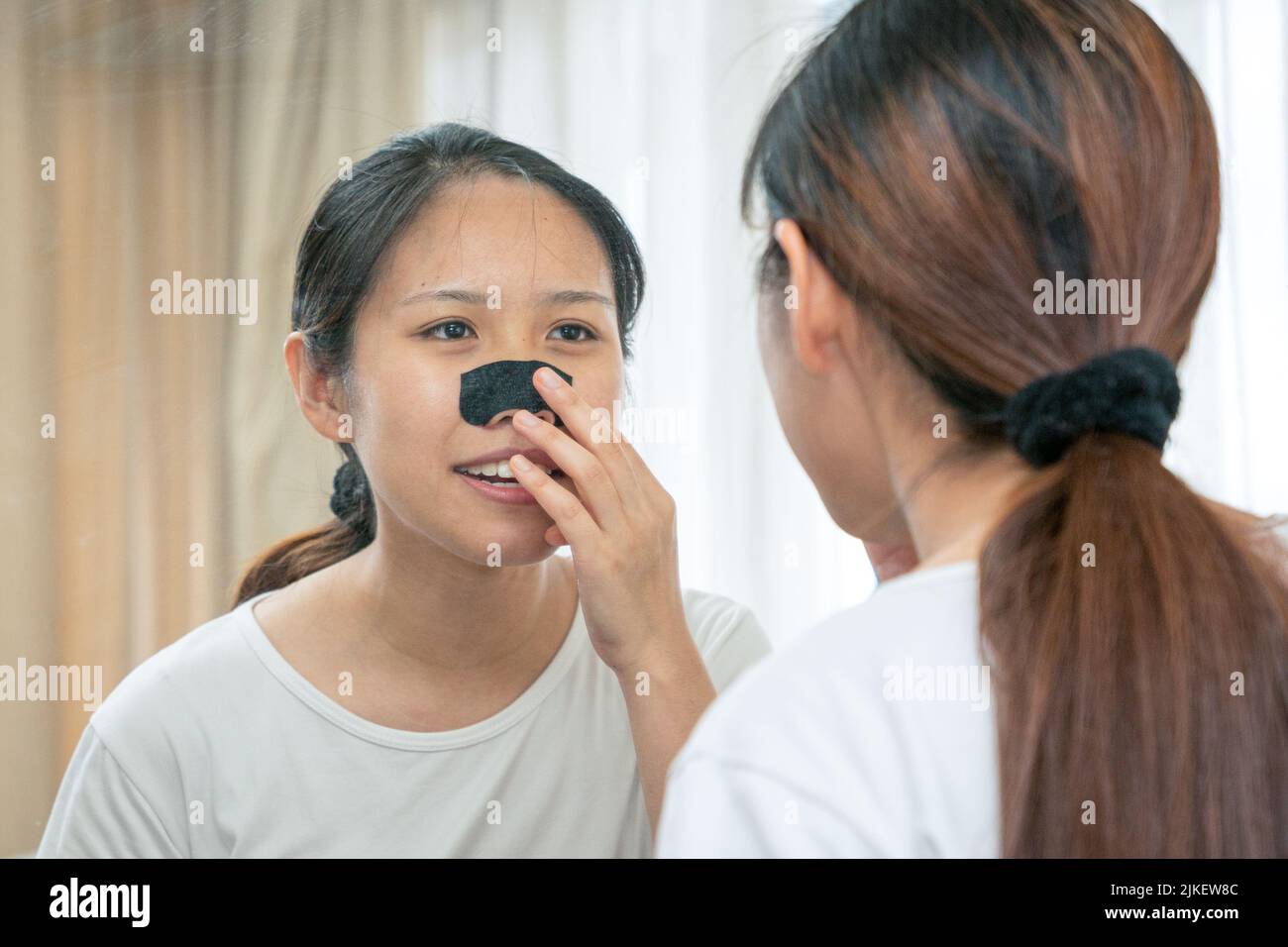 Belle femme asiatique regardant le miroir, appliquant le masque charbon de bois nettoyage profond nez bande de pore sur la peau propre fraîche. Soins de beauté et de soin de la peau Banque D'Images