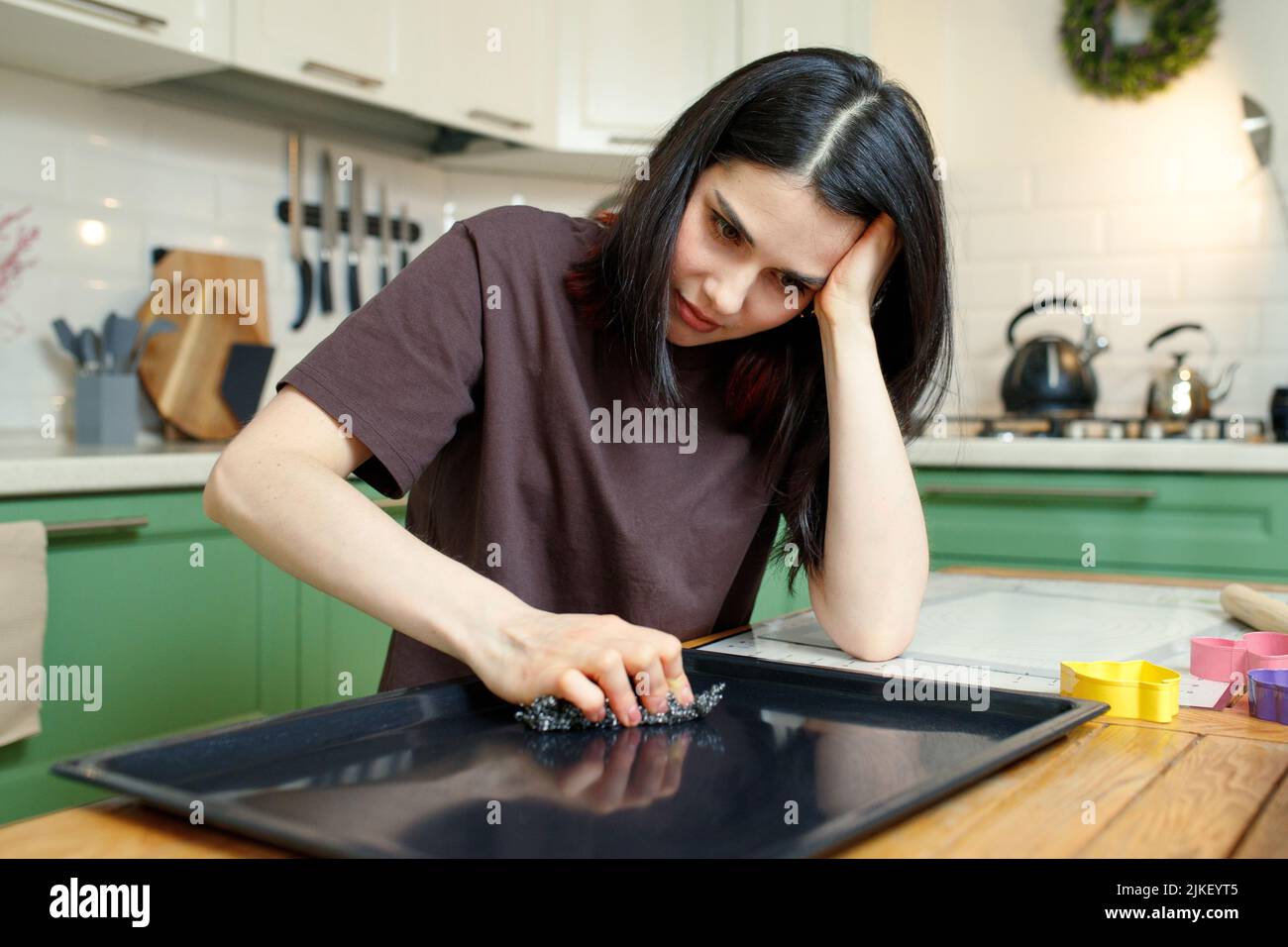 La femme bouleversée nettoie une plaque de cuisson dans la cuisine, fatiguée des tâches ménagères. Banque D'Images