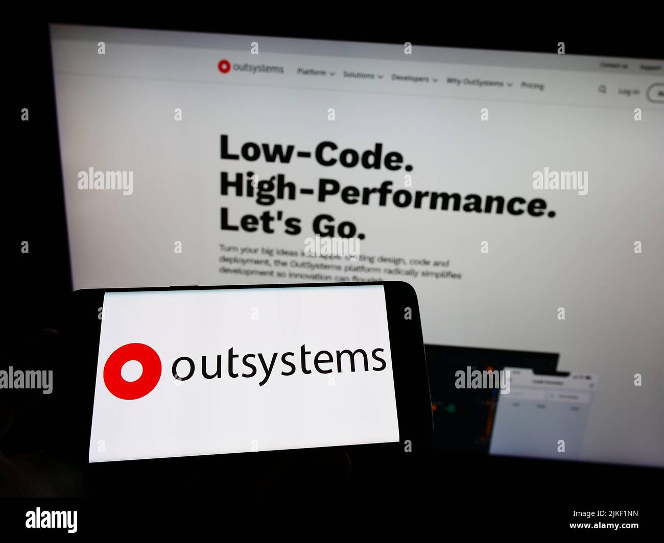 Personne tenant le téléphone portable avec le logo de la société de logiciel à code faible OutSystems à l'écran devant la page Web d'affaires. Mise au point sur l'affichage du téléphone. Banque D'Images