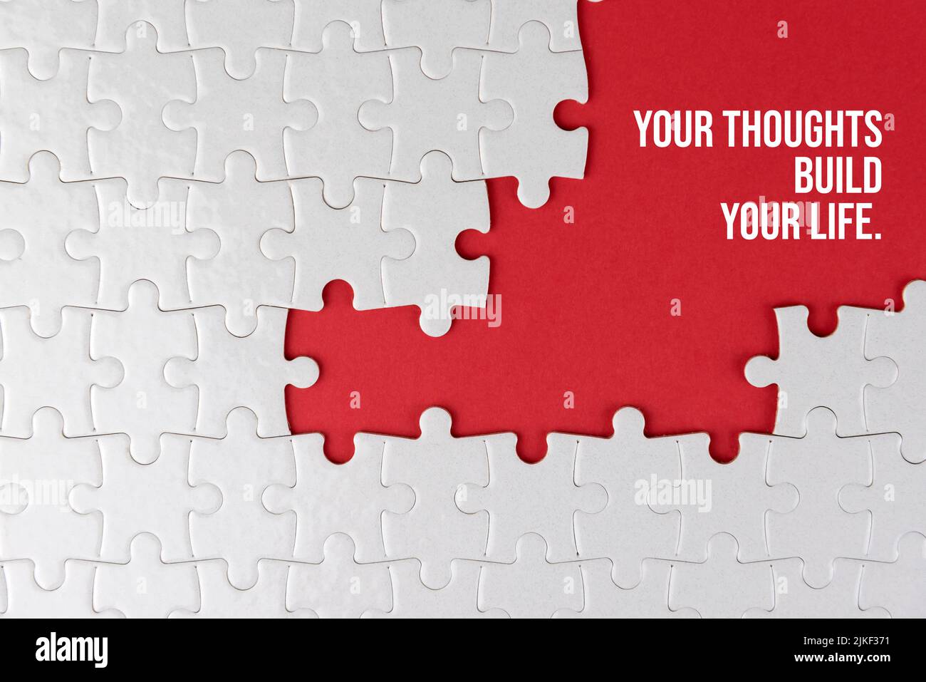 Citation inspirante et motivationnelle de la vie - vos pensées construisent votre vie. Avec puzzle blanc avec quelques pièces manquantes sur fond rouge. Banque D'Images