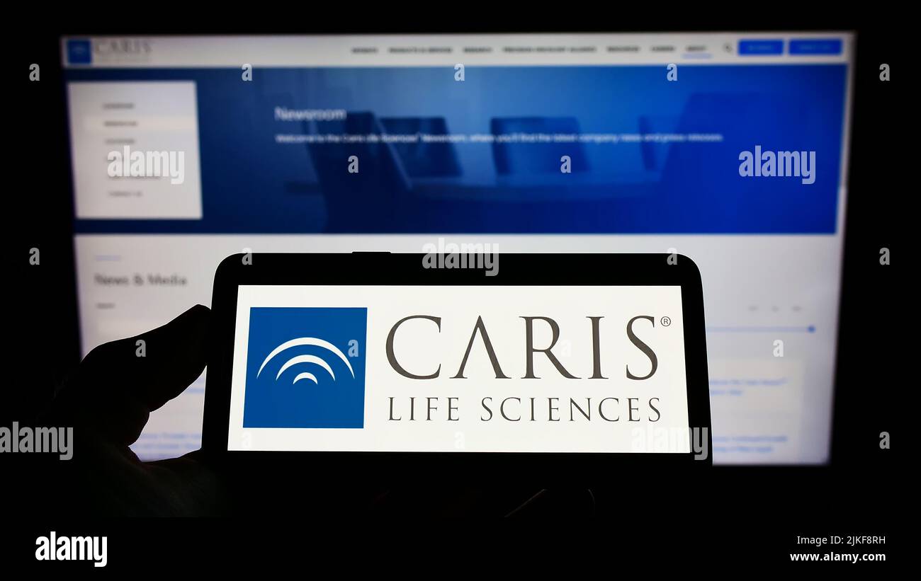 Personne tenant un téléphone portable avec le logo de la société américaine de biotechnologie CARIS Life Sciences à l'écran en face de la page web. Mise au point sur l'affichage du téléphone. Banque D'Images