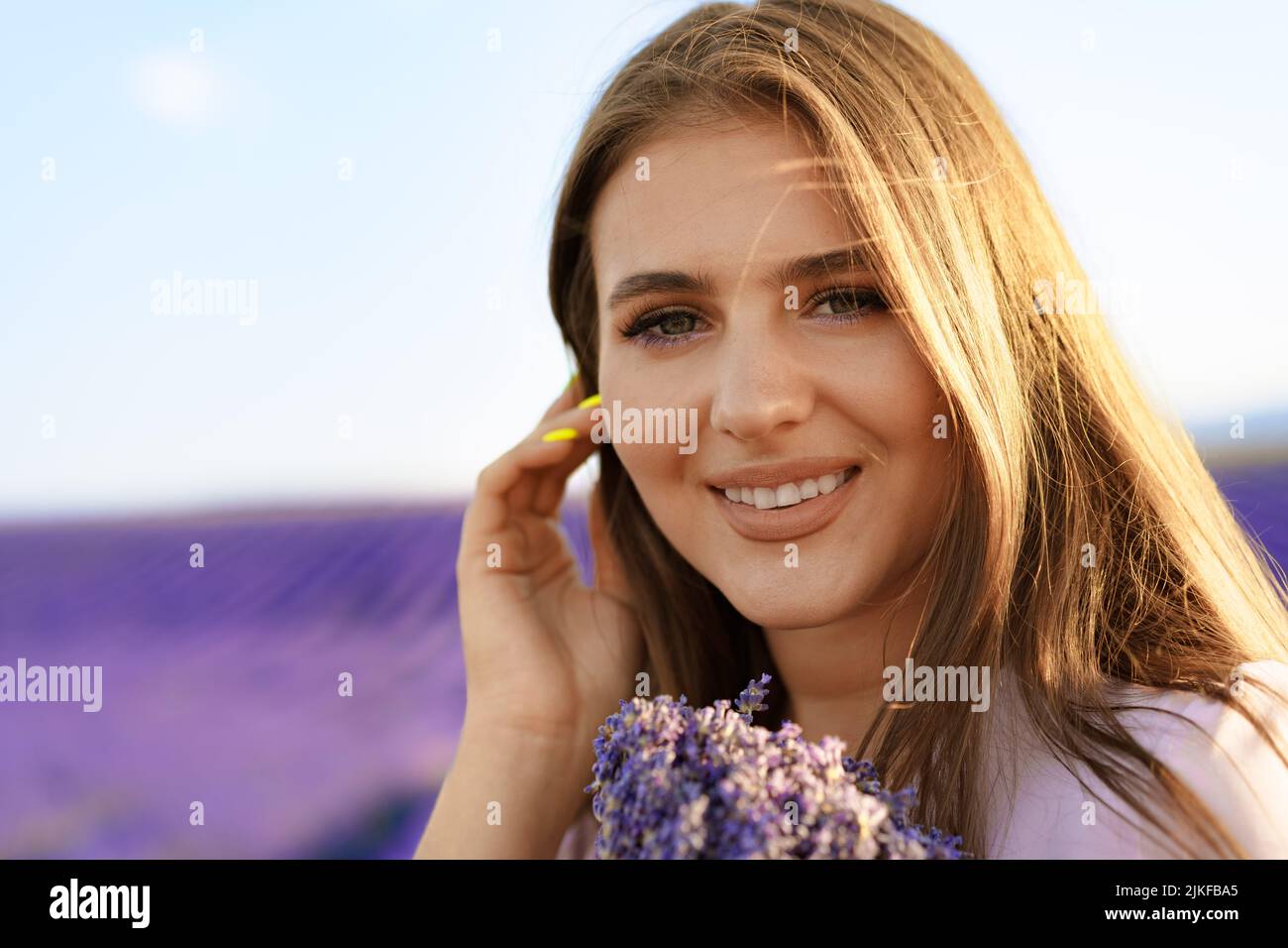 Jeune femme en robe tenant un bouquet de fleurs debout dans le champ de lavande Banque D'Images