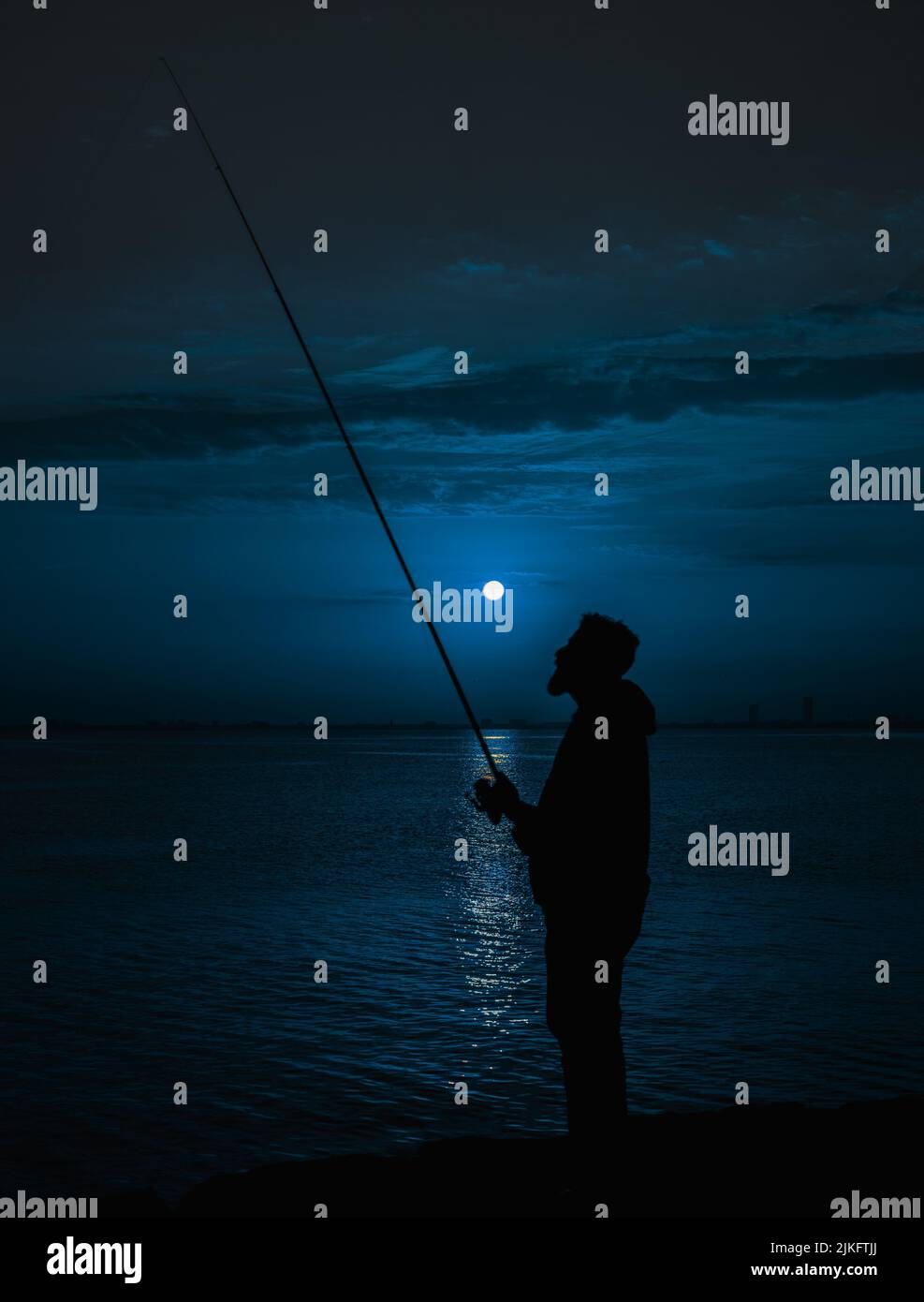 Un homme pêchant sur une rivière sous la lune Banque D'Images
