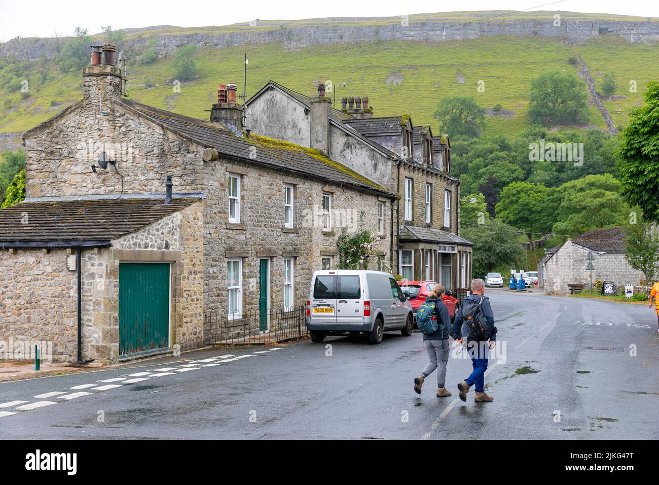 Kettlewell village dans les Yorkshire Dales, deux adultes marchant et faisant de la randonnée dans le village portant des sacs à dos, Yorkshire, Angleterre, Royaume-Uni Banque D'Images