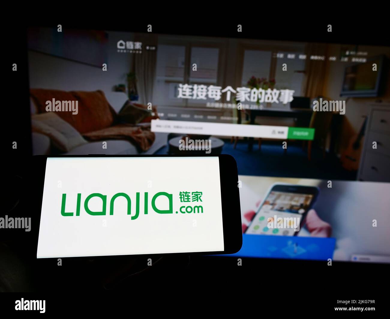 Personne tenant le téléphone mobile avec le logo de la société immobilière chinoise Lianjia sur l'écran en face de la page Web d'affaires. Mise au point sur l'affichage du téléphone. Banque D'Images