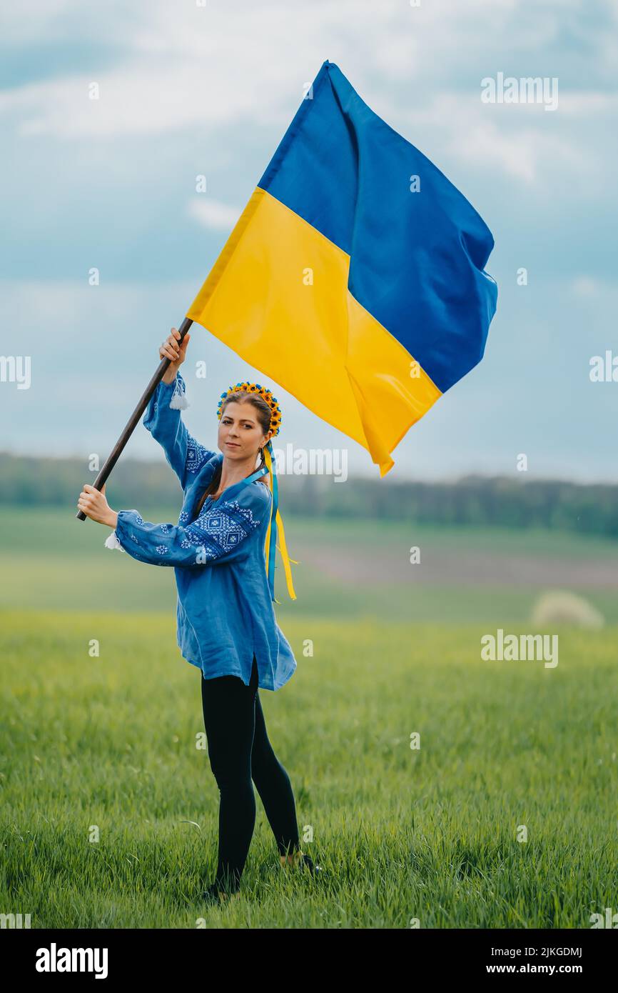 Belle femme ukrainienne avec drapeau national sur fond de champ vert. Jeune femme en bleu broderie vyshyvanka. Ukraine, indépendance, liberté Banque D'Images