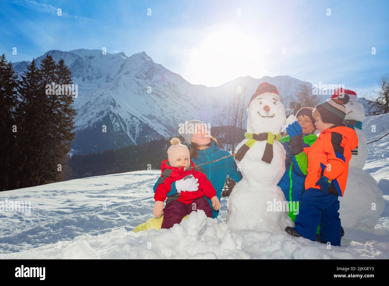 Famille avec mère, fille et deux garçons construire bonhomme de neige dans les montagnes Banque D'Images