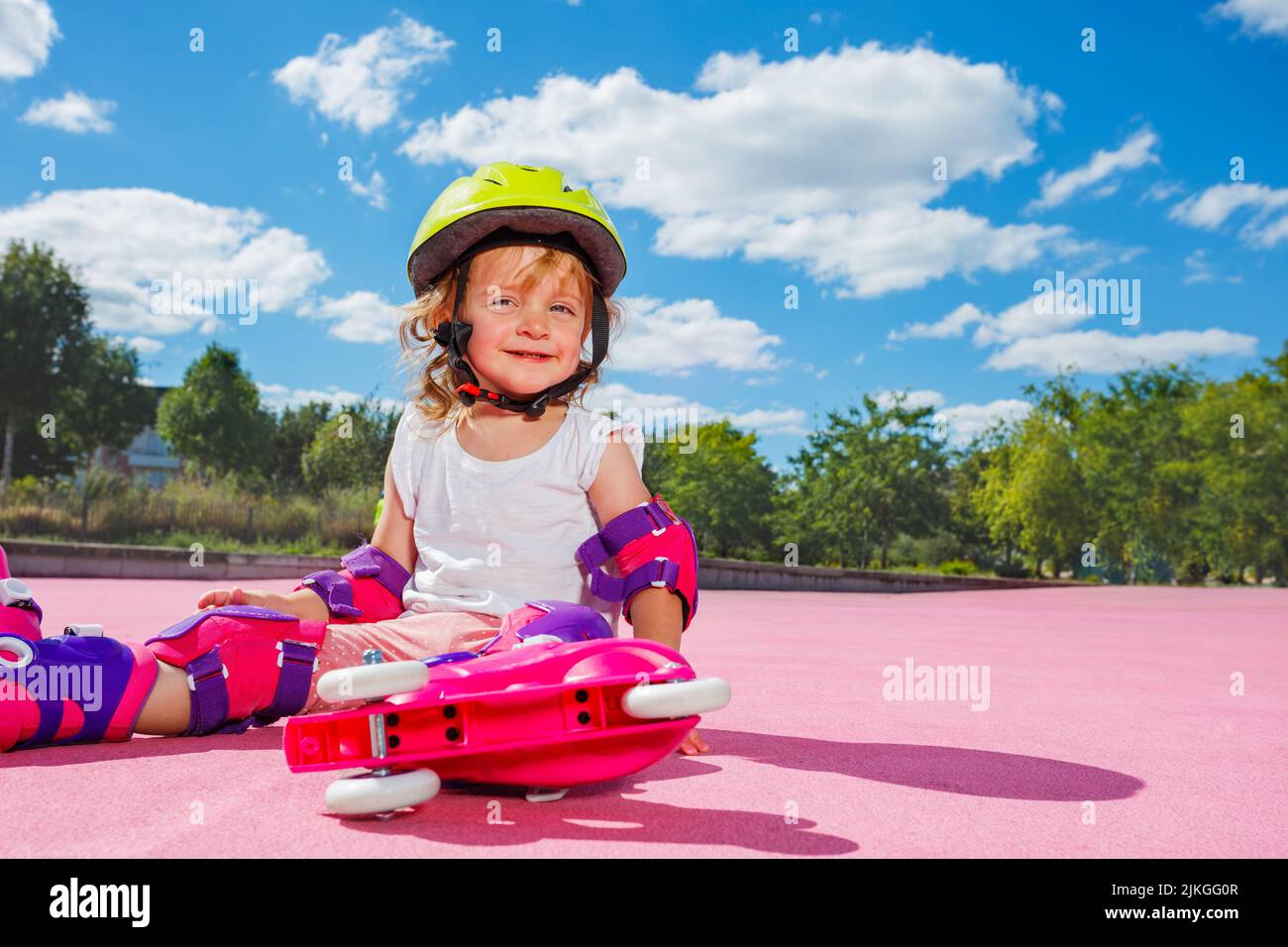 Jolie fille apprendre à utiliser des rouleaux, s'asseoir souriant au skate Park Banque D'Images