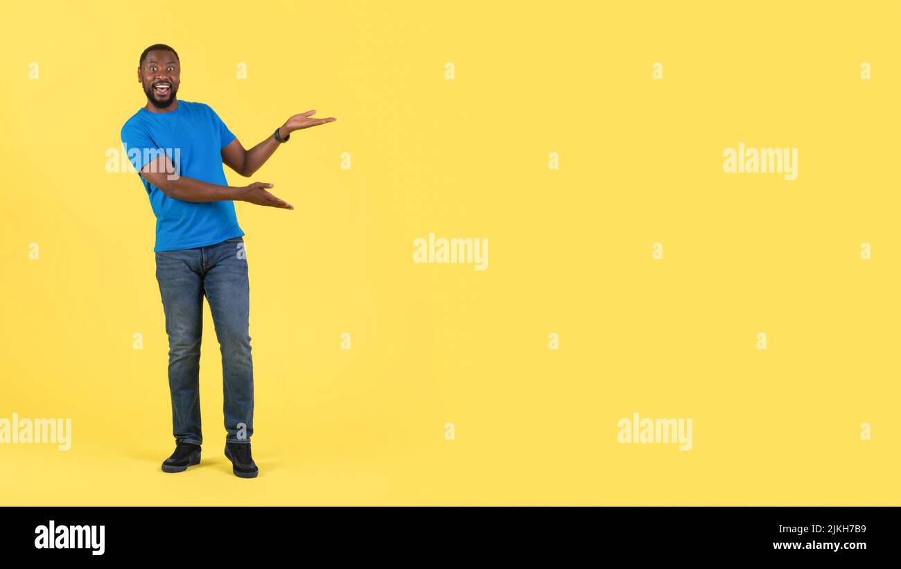 Un Black Guy excité qui fait un geste en pointant vers l'espace libre, fond jaune Banque D'Images