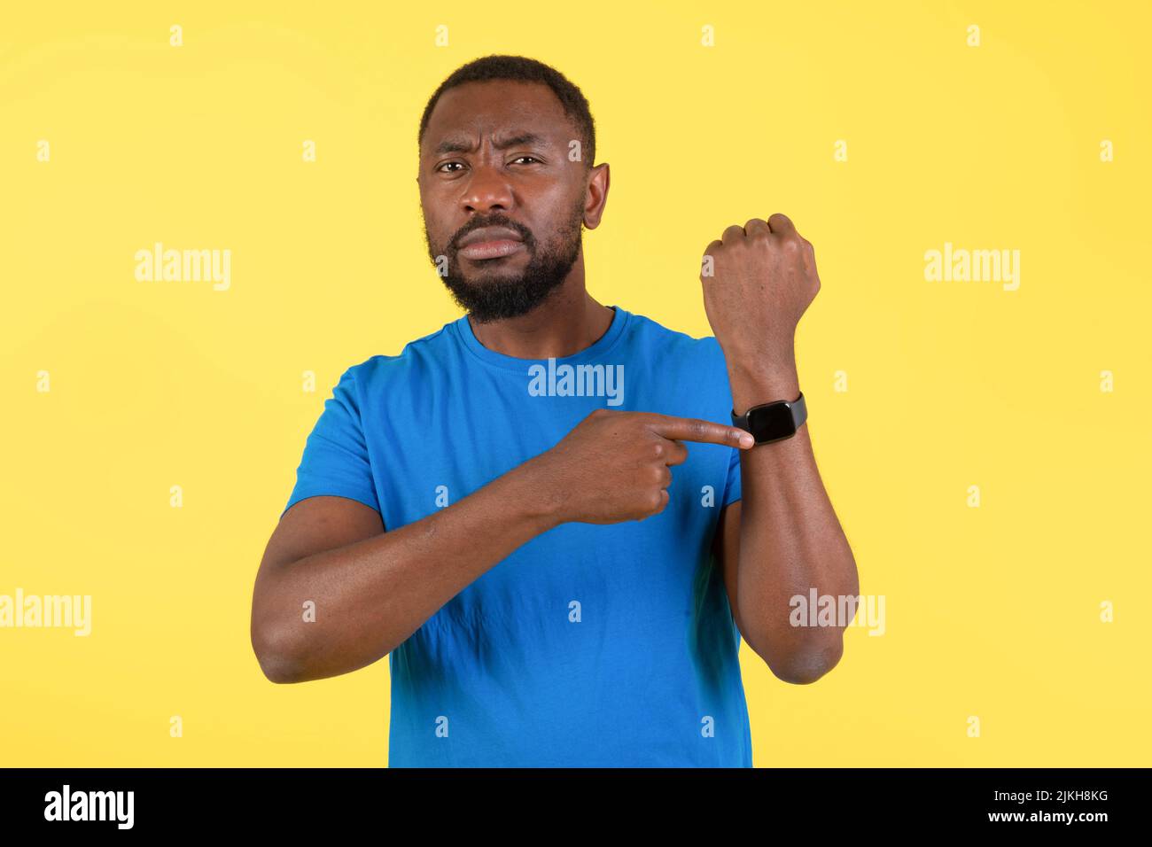 Un homme afro-américain mécontent montrant Smartwatch sur fond jaune Banque D'Images