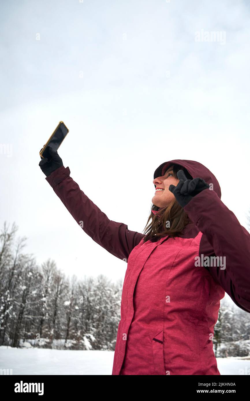 Une photo verticale d'une femme caucasienne gaie vêtue de vêtements roses prenant des selfies sous la neige Banque D'Images