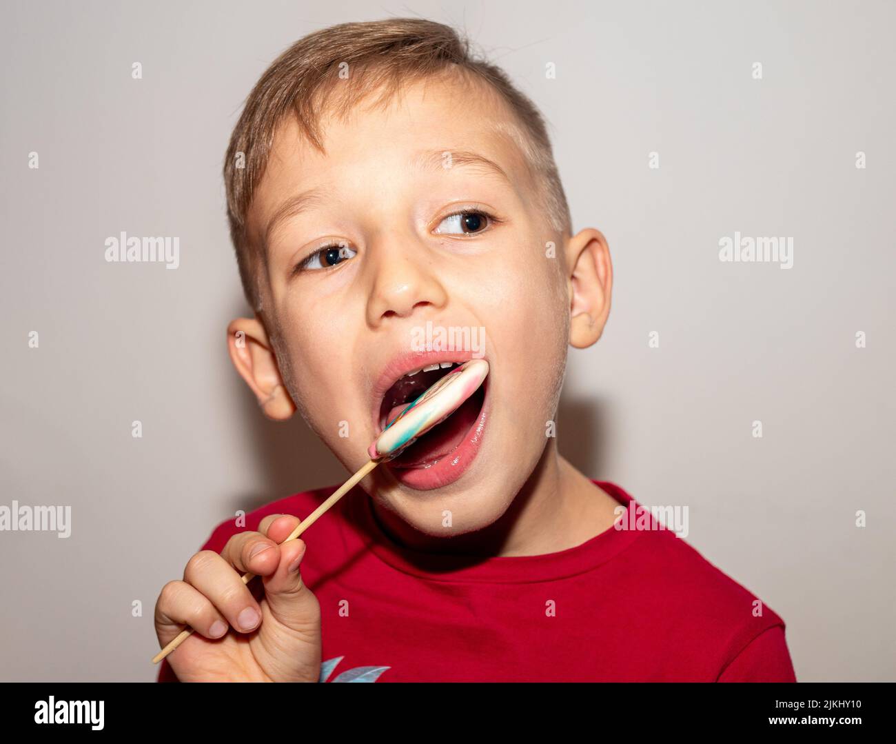 un garçon mange un bonbon multicolore sur un bâton, un garçon avec un bonbon de sucre qu'il tient dans ses mains Banque D'Images