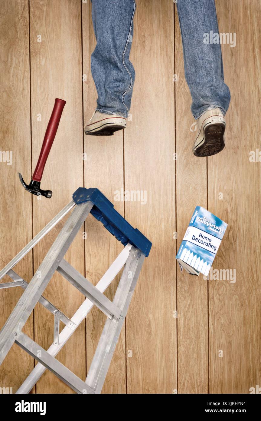 Un plan vertical d'un homme tombant de l'échelle avec un marteau et un guide livre sur la décoration de la maison Banque D'Images