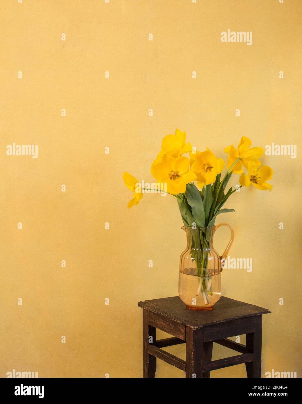 La paix se trouve à chaque coin de rue. Tulipes jaunes dans un vase pêche. Sur un tabouret brun foncé devant le fond jaune. Banque D'Images