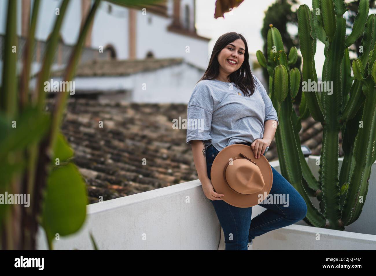Une vue d'une femelle caucasienne curvy avec un chapeau, souriant et posant contre un cactus Banque D'Images